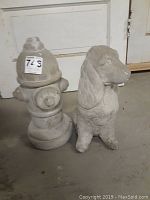 Concrete fire hydrant and dog figures placed on floor against a door, showing frontal view of both.