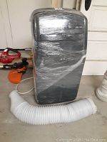 Front view of LG portable air conditioner wrapped in plastic with exhaust hose laid out