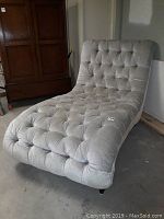Front angled view of gray tufted chaise lounge chair showing button tufting and fabric texture