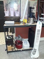 Shelf with Bella NutriPro juicer, four Honeywell fans, red crock pot, loaf pan, vases, mugs, and decorative chest.
