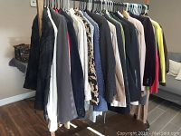 Side view of a rack holding several women's jackets and blazers in assorted colors and sizes, hanging on plastic hangers.