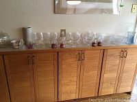 Clear crystal stemware and assorted glass items displayed on wooden sideboard, including various glasses and candles.