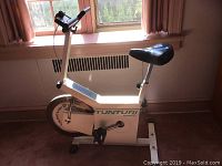 Full side view of white and green Tunturi stationary exercise bike showing black seat, pedals and handlebar mounts.