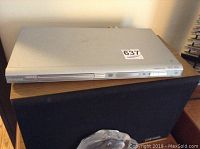 Front view of Phillips DVD player on wooden surface with a speaker below it.