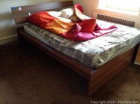 Wooden bed frame with headboard, footboard, and side rails, mattress with linens on top.