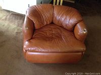 Front view of rust colored leather chair showing overall shape and damage on both arms.