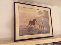 Framed print of two horses running in a natural landscape hung on a wall.