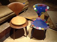 Two chairs side by side, one natural wood with cushion and one painted blue with multicolor circles