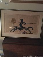 Framed print depicting Don Quixote figure with lance and circular sun motif.