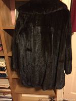 Back view of the dark mink fur coat hanging on a shelf, showing texture and length