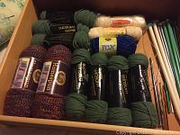 Overhead view of drawer containing various yarn skeins, knitting needles, and crochet hooks.