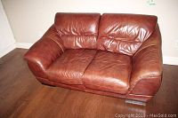 Front-facing view of brown leather loveseat showing two seats and cushioned armrests.