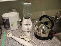Photo showing Braun juicer, Osterizer blender with glass pitcher and whisk, Braun hand blender, and Philips electric kettle all placed on a kitchen counter.