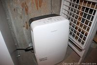 Garrison white dehumidifier and white metal drying rack in a basement corner with concrete floor and wall.