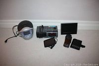 Sony Dream Machine clock radio with CD player, Sanyo clock radio, TomTom GPS with charging cable, two BlackBerry phones with cases, digital photo frame arranged on floor.