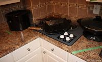View of countertop showing Breville electric wok, nonstick grill pan, BBQ grill pan, stove control knobs, and kettle in the corner.