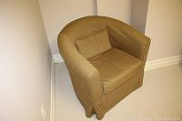 Front view of the beige upholstered tub chair with a small cushion on the seat, showing the rounded back and armrests, and fabric skirt covering the legs.