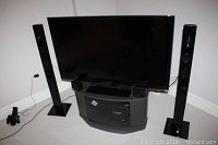 Front view of Panasonic TV on Sony stand with two speakers on carpeted floor.