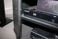 Close-up of Samsung Blu-ray 3D player on black shelf with visible Samsung branding and disc tray.
