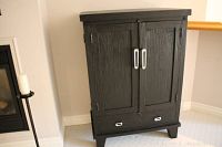 Full view of the stained cherrywood storage cabinet showing front with two doors and bottom drawer.