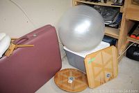 Two wooden balance boards (round and square) placed on the floor leaning against a plastic bin, with a silver exercise ball on top of the bin.