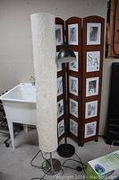 Tall white cylindrical paper lamp next to black metal lamp and folding photo frame screen