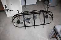 Full view of hand forged black metal pot hanger on floor showing the frame, hooks, and decorative grape leaves.