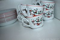 Photo of stacked holiday themed cups with festive designs of Santa Claus and sleigh, showing detail of pattern and red rim.