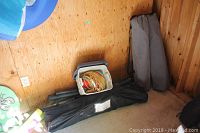Photo showing plastic bin with hammock fabric and two folded camp chair bags alongside black hammock frame parts and carrying case on floor against wood wall.
