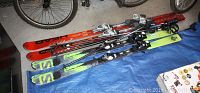 Two pairs of skis and ski poles laid on blue tarp in garage