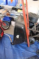 Side view of the black Jobmate steel wheelbarrow showing the red handles and single wheel.