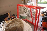 Two red Winnwell hockey nets standing upright in a garage setting next to various household items like a basket and cooler.