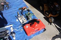 Wide view of tools laid out on blue tarp including Milwaukee battery charger and case, Bosch drill, Black & Decker sander, Mastercraft grinder, cords and light fixtures.