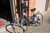 Full view of the bicycle leaning against a garage wall showing frame and overall condition.
