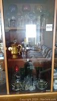 Wooden display cabinet holding the lot items including glassware and brass pitcher