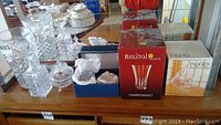 Photo showing an assortment of crystal glass items including decanter, candy dishes, cut glass vase, and boxed glasses on wooden shelf.