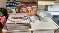 Overview of lot showing Corning Ware casserole dish, canister set box and Salad Queen box on a kitchen counter.