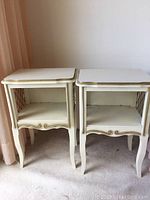 Both cream bedside tables with gold trim next to each other showing front and sides