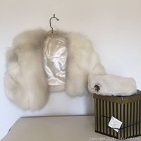 Full view of mink stole hung next to matching fur hat on striped box