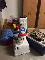Camping gear including sleeping bag, portable potty, ice chests, flashlights, water jug, kettle, and bag.