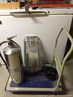 Full view of water fire extinguisher, metal trolley, hose attachment, and coiled accessory on trolley base.