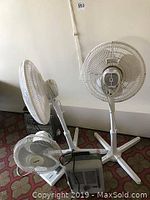 Three Holmes floor fans and two floor heaters on floor against wall.