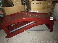 Side view of one red metal car ramp placed on concrete floor near boxes.