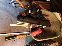 Wheelbarrow containing chimney sweep tube and two electric hedge trimmers inside. Concrete floor background.