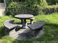 Full view of concrete garden set outdoors including round table on pedestal and three curved benches attached to base platform