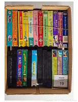 Top-down photo of a box containing 24 assorted children's and family VHS movies and TV shows.