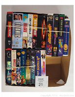 Photo of 19 assorted VHS movies stacked in a cardboard box showing spines with titles and movie artwork