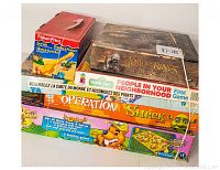Top view of stacked board games and puzzles showing Lord of the Rings, Shrek Operation, Fisher-Price Go Fish, Sesame Street, and world map puzzle with rubber bands