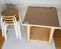 Photo of square wooden end table with lower shelf and four round wooden stools with white metal legs stacked together