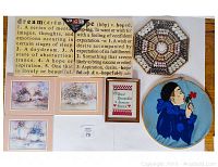 Display of various framed paintings and embroidery arranged on a white surface, including inspirational text embroidery, landscapes, cross-stitch sampler, round portrait embroidery, and a hexagonal mosaic piece.